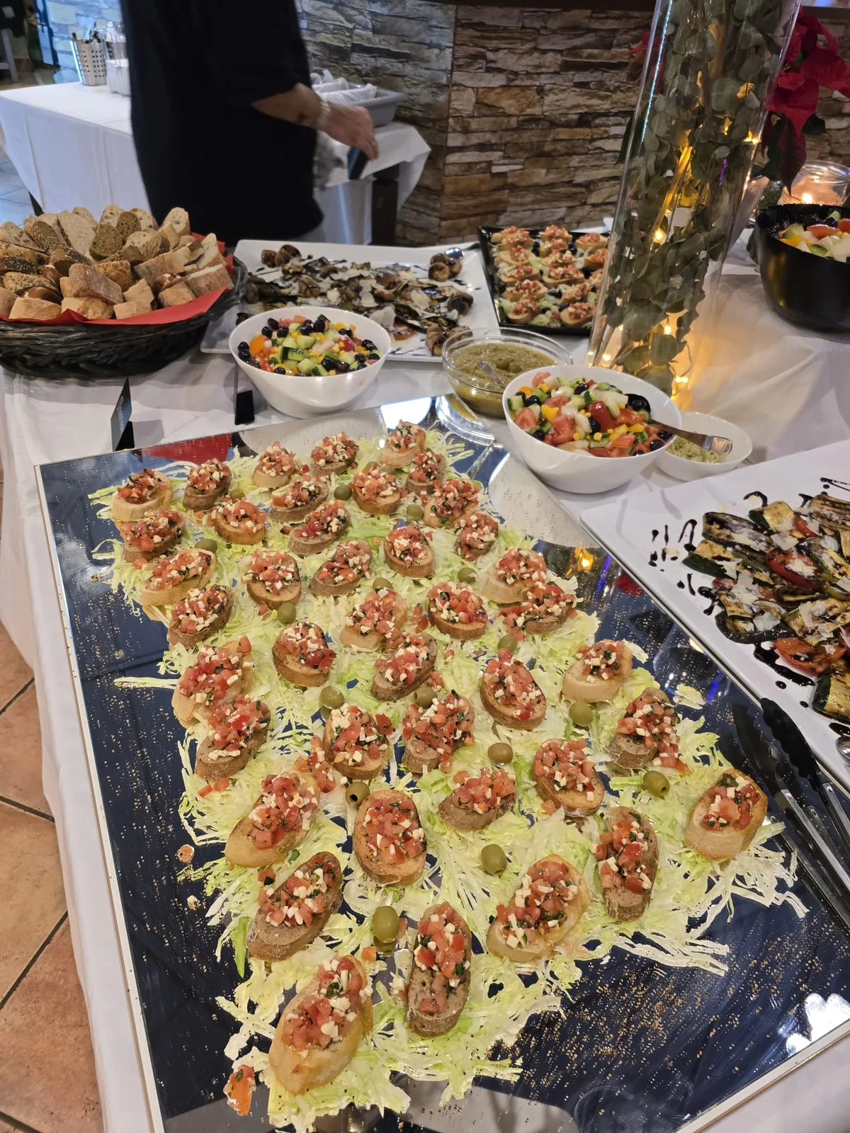 Platte mit Bruschetta, dahinter Brotkorb, Salate und Dips