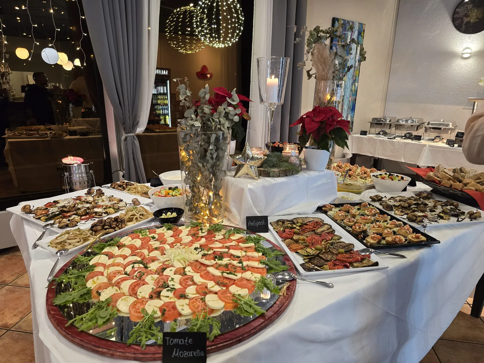 Buffet mit Caprese-Platte, Antipasti und Chafing-Dishes im Hintergrund