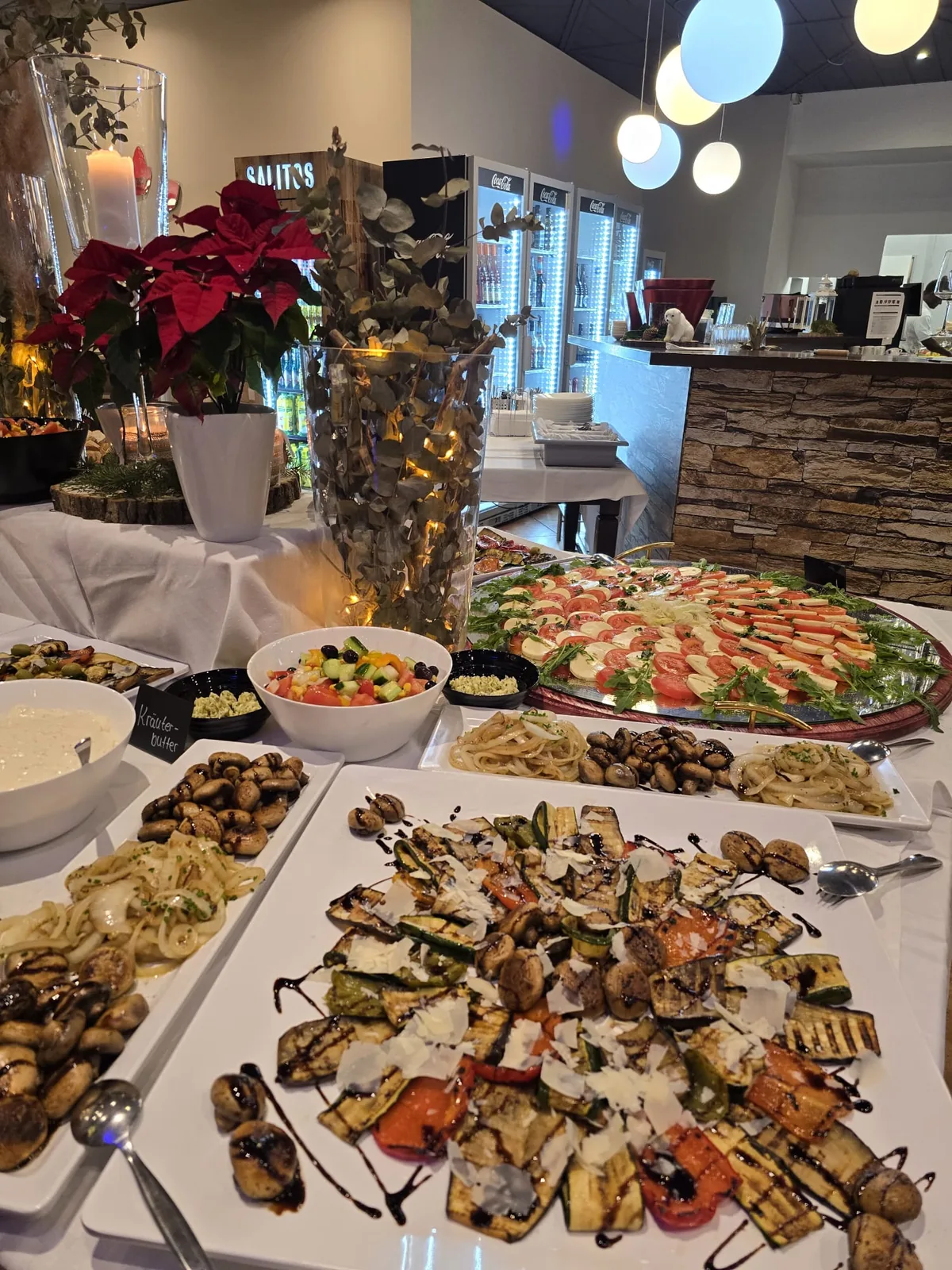Gegrilltes Gemüse mit Parmesan, dahinter Caprese-Platte an der Theke
