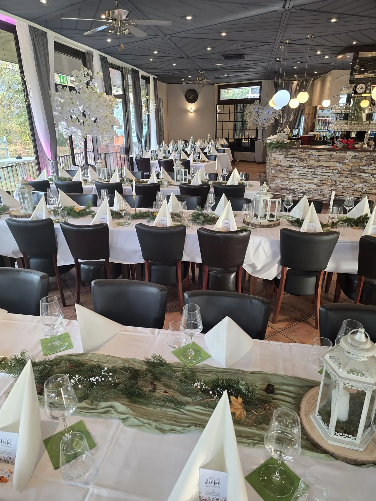 Festlich eingedeckter Saal mit langen Tafeln, weißen Blütenbäumen und Natursteintheke